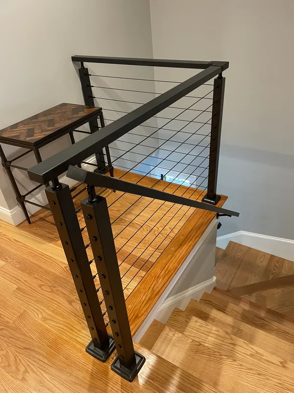 Black cable railing around a wood stair landing