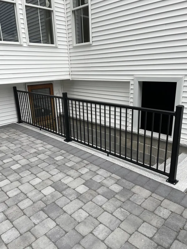 Black vertical-baluster railing beside a paved outdoor terrace