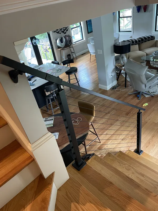 Cable railing with black posts viewed from the top of an interior staircase