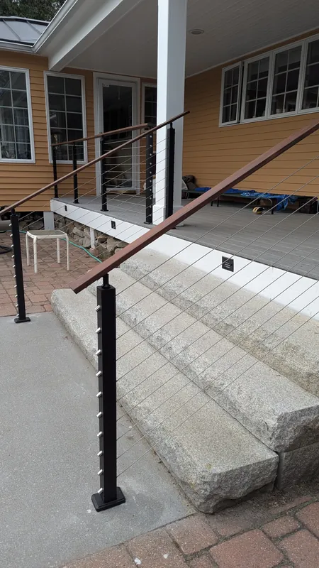 Exterior cable railing with black posts and wood handrails beside stone steps