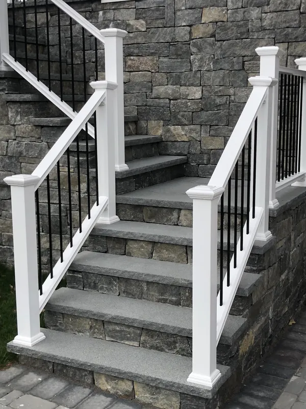 White stair railing with black vertical balusters beside a stone facade