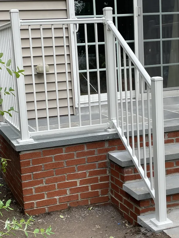 White railing around an entry landing above a brick foundation